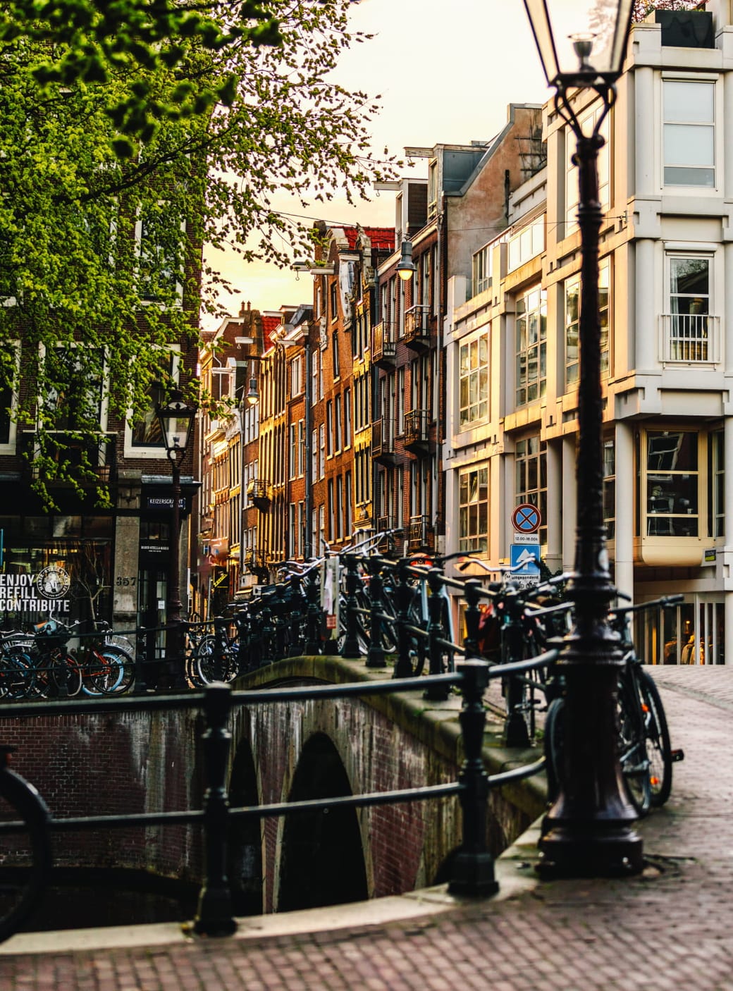 Bicycles parked along a canal bridge beneath an old street lamp, with canal houses behind