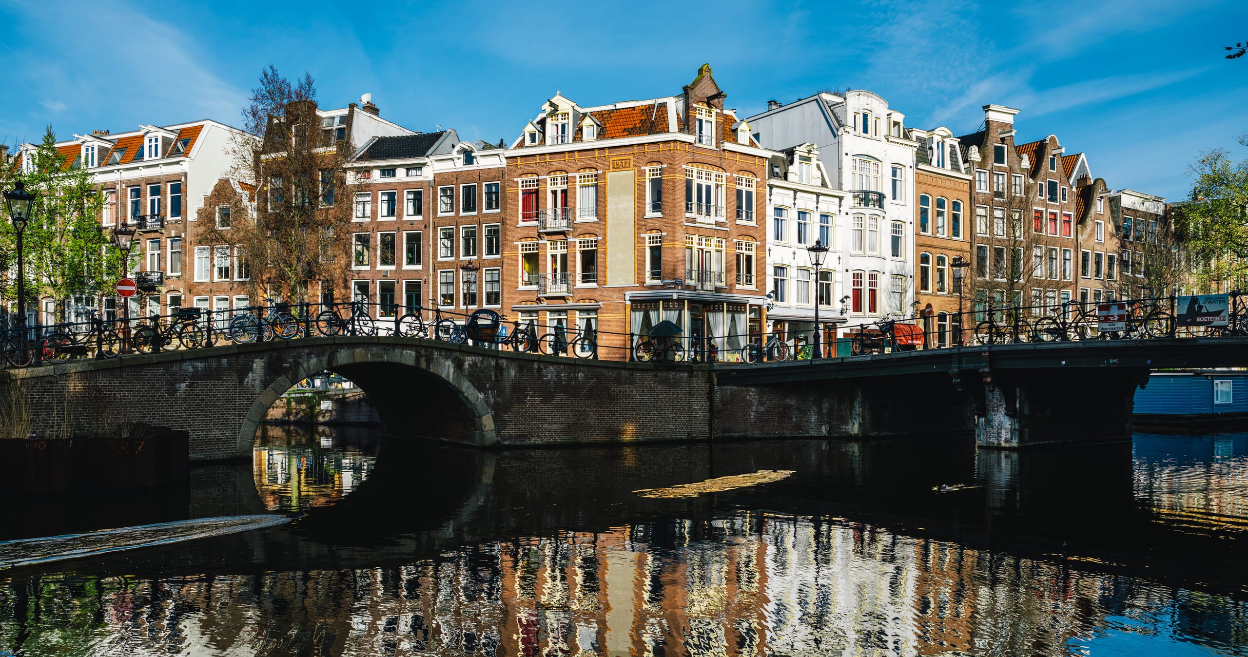 Amsterdam canal houses and an arched stone bridge mirrored in the still water of the canal