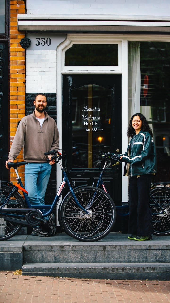 Two people with a bicycle at the front door of an Amsterdam canal house