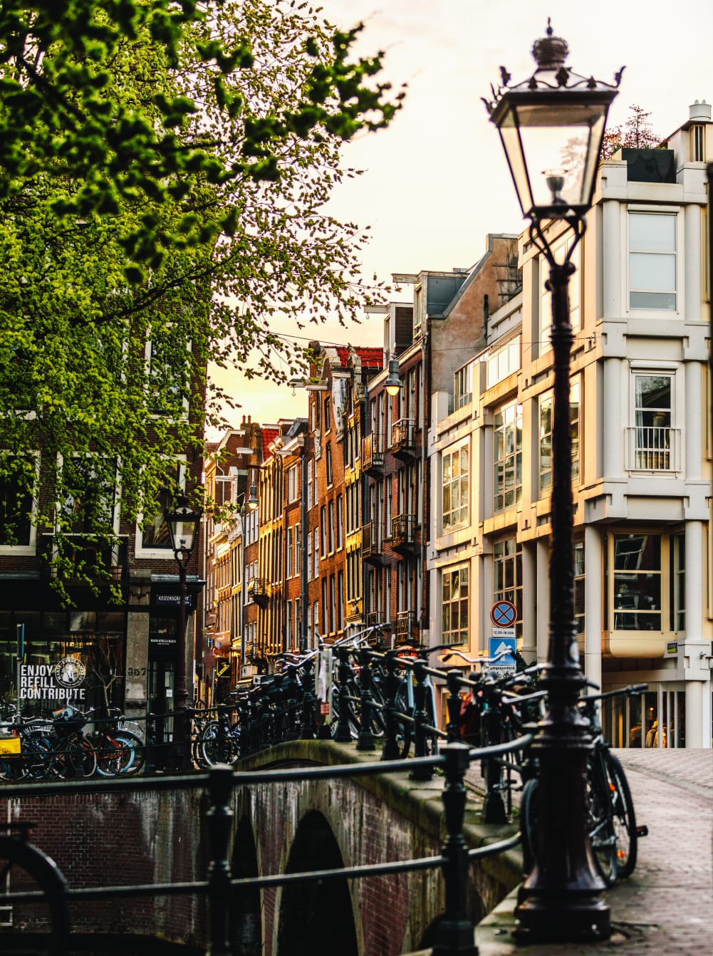 A canal-side street in Amsterdam, with a lamppost and bicycles parked along the bridge railings