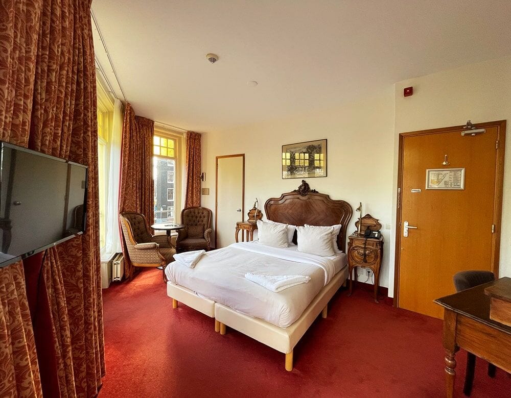 Double Room with Canal View: the bed, armchairs and windows onto the canal
