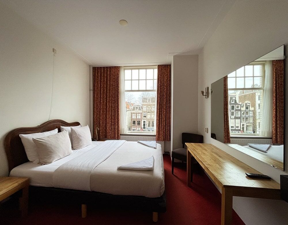 Small Double Room: double bed with a wooden headboard beneath a window onto canal houses