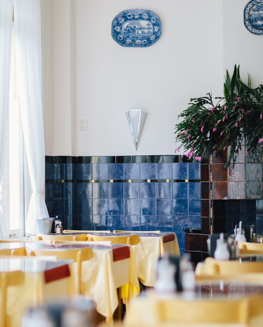 The hotel's breakfast room, tables laid with yellow linen beneath Delft blue tiles
